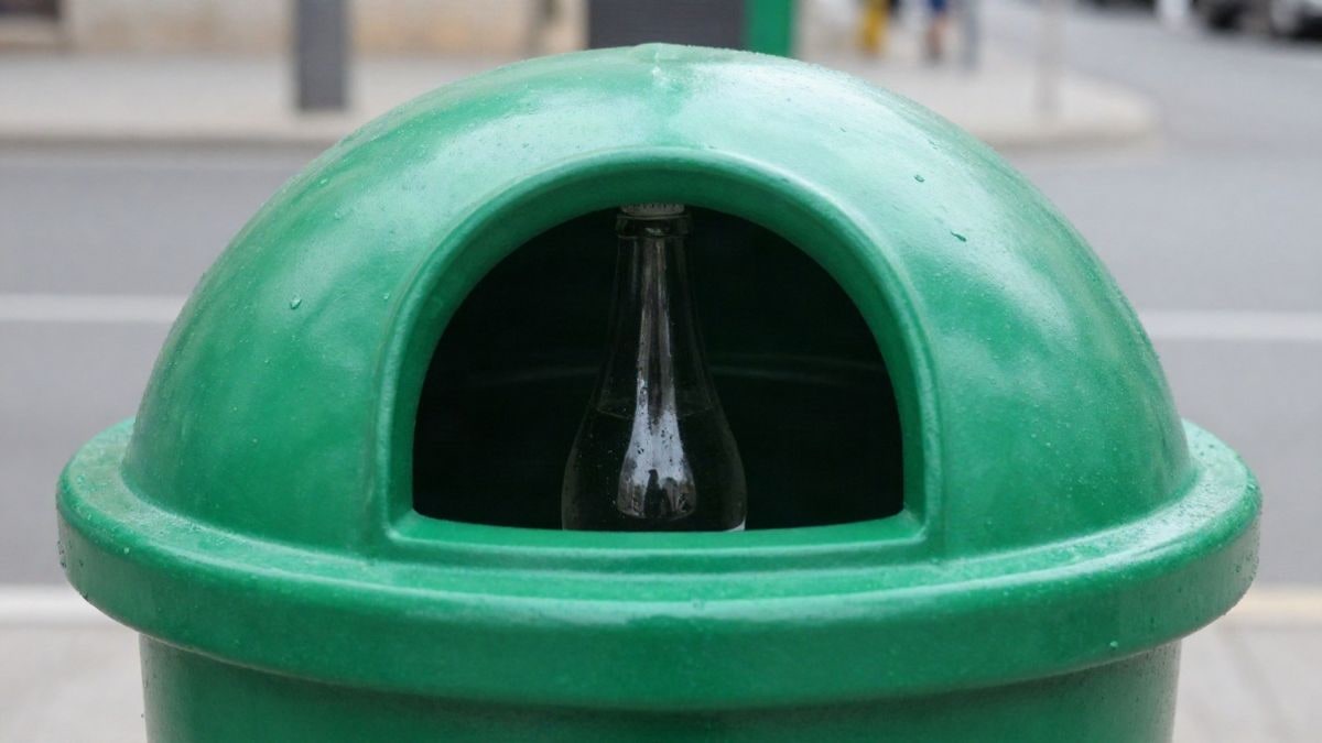 Imagen ilustrativa: primer plano de una botella de vidrio en un contenedor de reciclaje verde