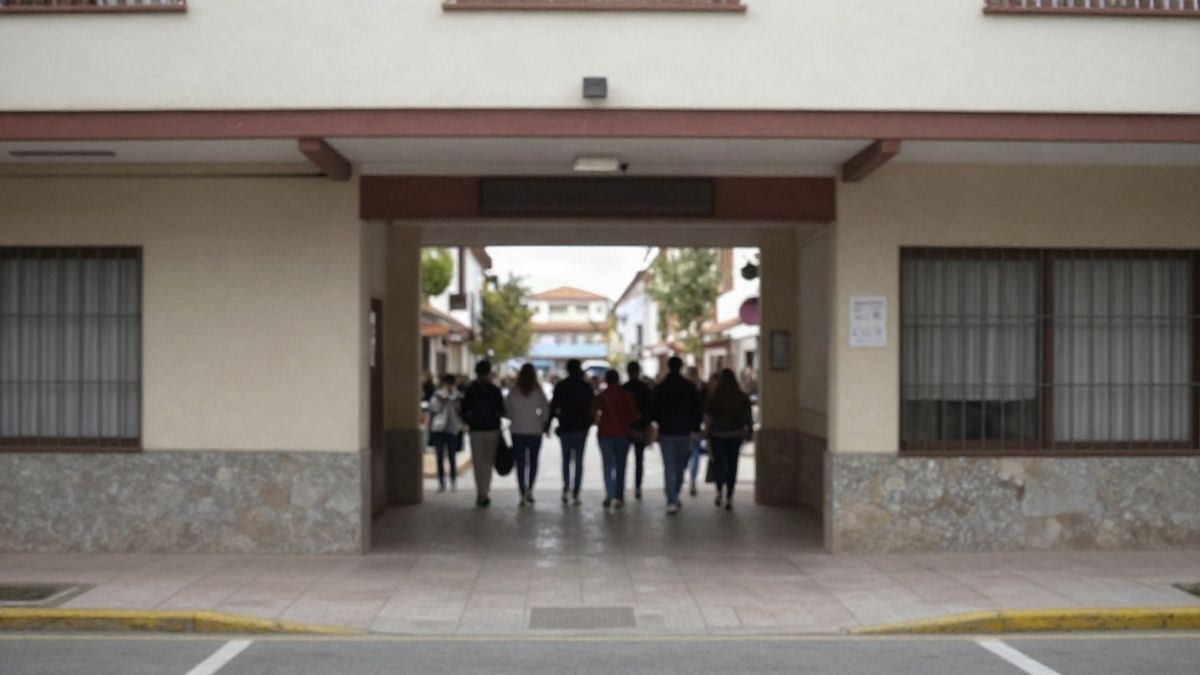 Imagen ilustrativa: entrada de una escuela con mochilas colgadas y algunos padres de fondo, en un día nublado.