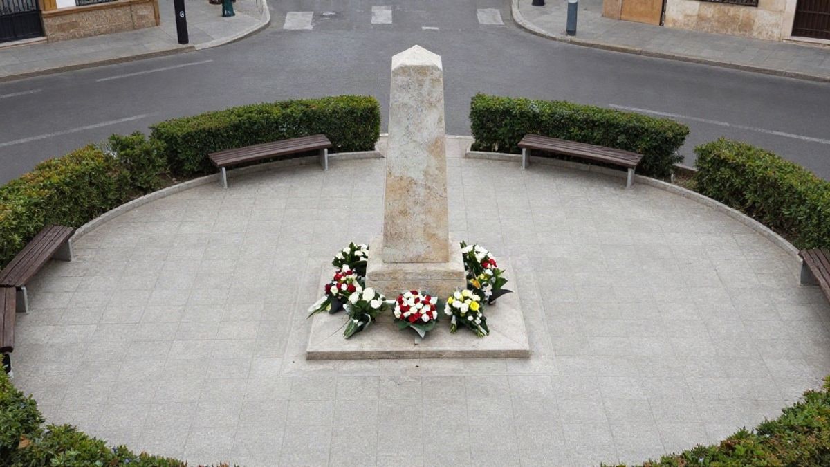 Imagen ilustrativa: vista cenital de un monolito de piedra con flores en una plaza ajardinada