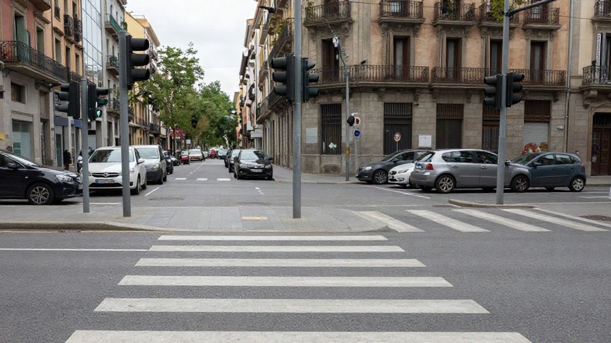 Imagen ilustrativa: cruce urbano corriente con semáforos, paso de peatones y coches aparcados en un día nublado