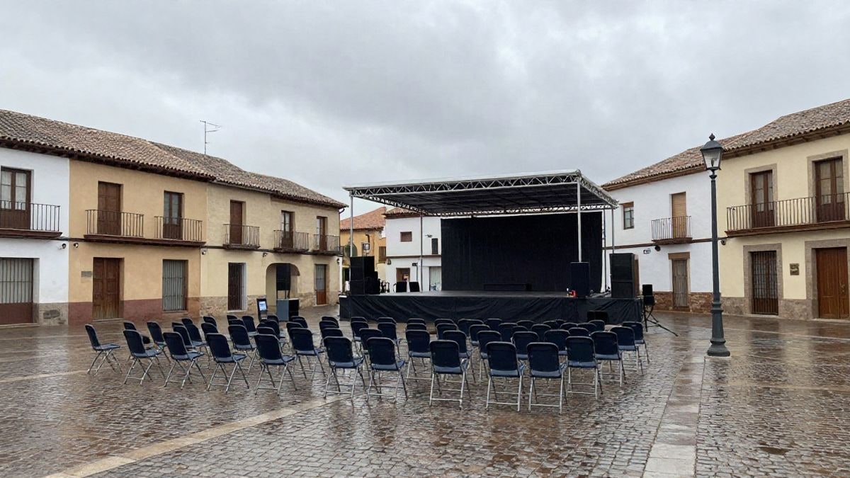 Imagen ilustrativa: plaza empedrada con sillas plegables y un escenario montado para una fiesta al aire libre bajo un cielo encapotado