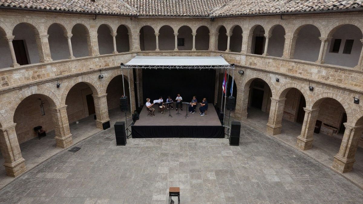 Imagen ilustrativa: vista cenital de un claustro de piedra con arcos y un pequeño escenario preparado para un concierto familiar