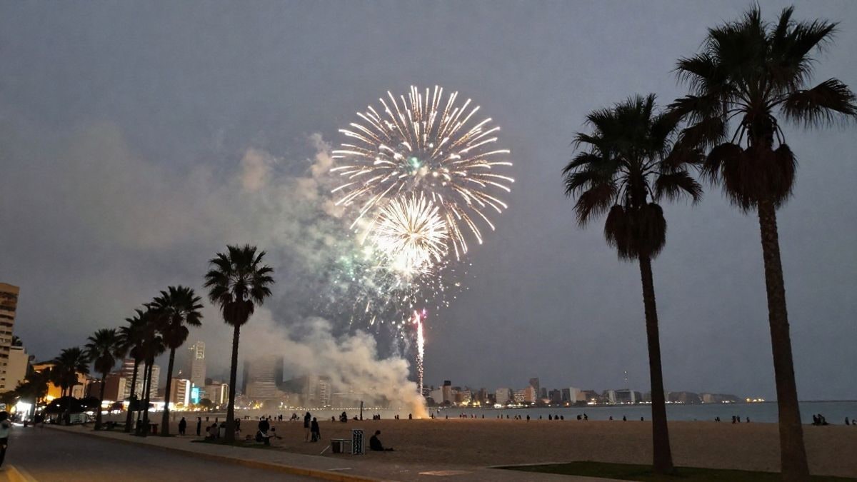 Imagen ilustrativa: fuegos artificiales en el cielo nocturno sobre una playa urbana con palmeras y rascacielos al fondo
